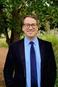 Jonathan Dodson's headshot. He is wearing a blue blue dress with a navy tie and jacket and gray glasses.